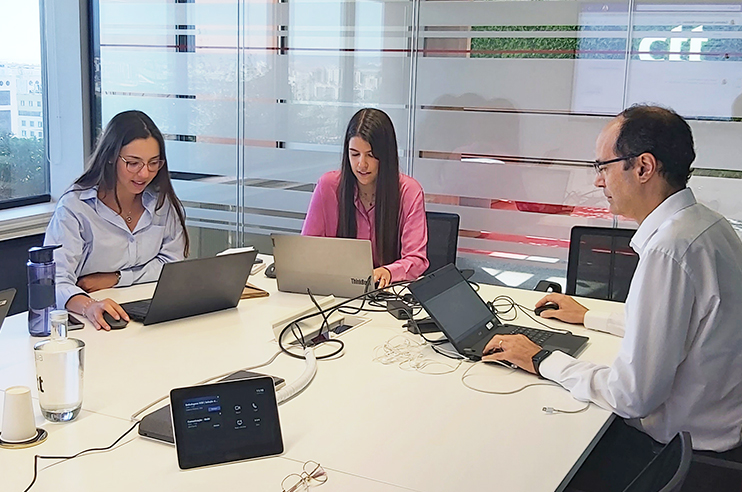 três pessoas sentadas numa mesa a trabalhar no computador